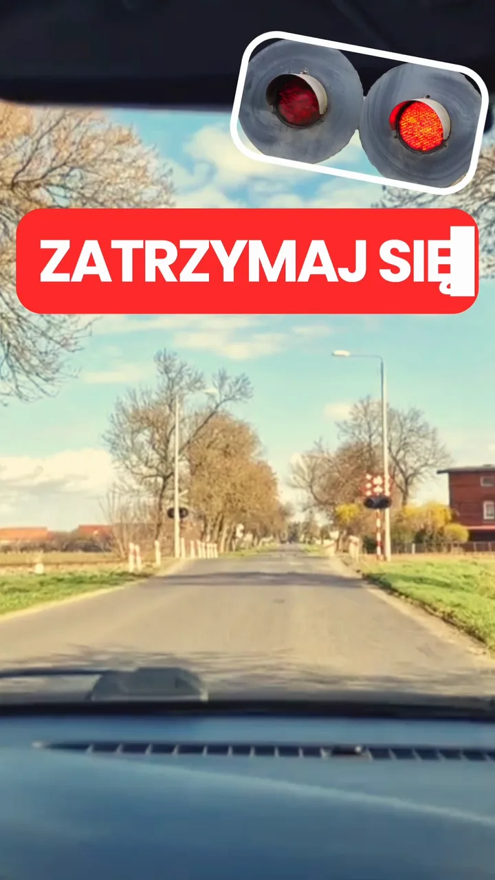 Droga prowadząca do przejazdu kolejowo-drogowego z napisem „ZATRZYMAJ SIĘ” i sygnalizatorem z czerwonym światłem.